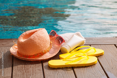 Hat, sunglasses and sunscreen at the side of swimming pool, summer travel concept