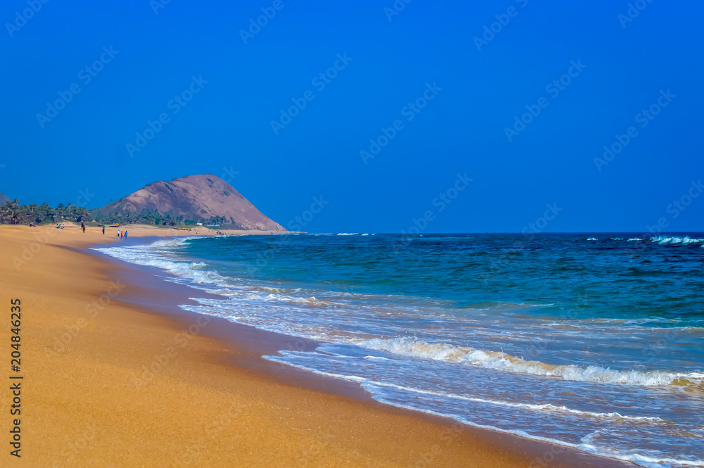 Wild Empty Tropical beach, vibrant yellow sand, bright blue sky, crystal clear waters with water crashing on the shore at daytime on a sunny day