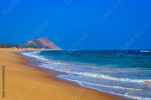Wild Empty Tropical beach, vibrant yellow sand, bright blue sky, crystal clear waters with water crashing on the shore at daytime on a sunny day