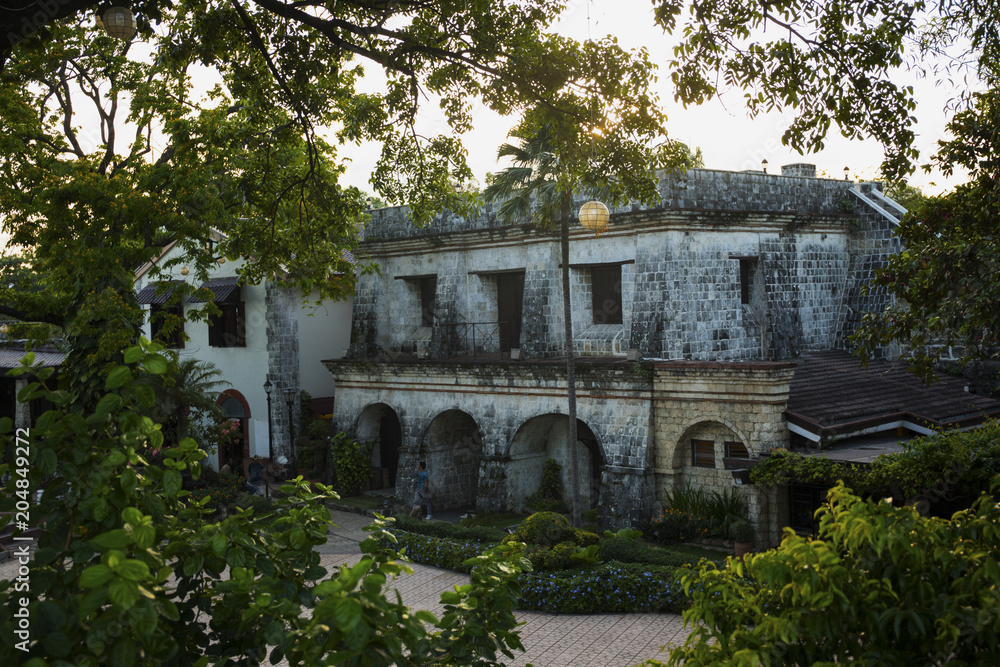 Obraz premium Old historic house view through tropical plants. Fort San Pedro view in sunset. Oldest historical fort in Philippines.