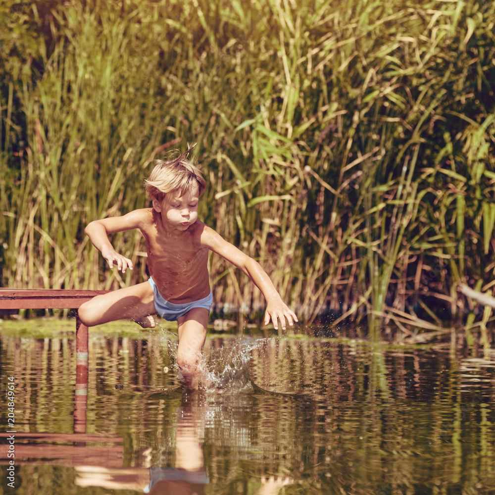 Little boy having fun and jumping into the river from pier, image with square aspect ratio and warm toning Little boy having fun and jumping into the river from pier, image with square aspect ratio and warm toning