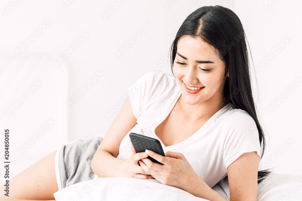 Happy woman relaxing and using smartphone on the bed at home.woman checking social apps with smartphone Happy woman relaxing and using smartphone on the bed at home.woman checking social apps with smartphone