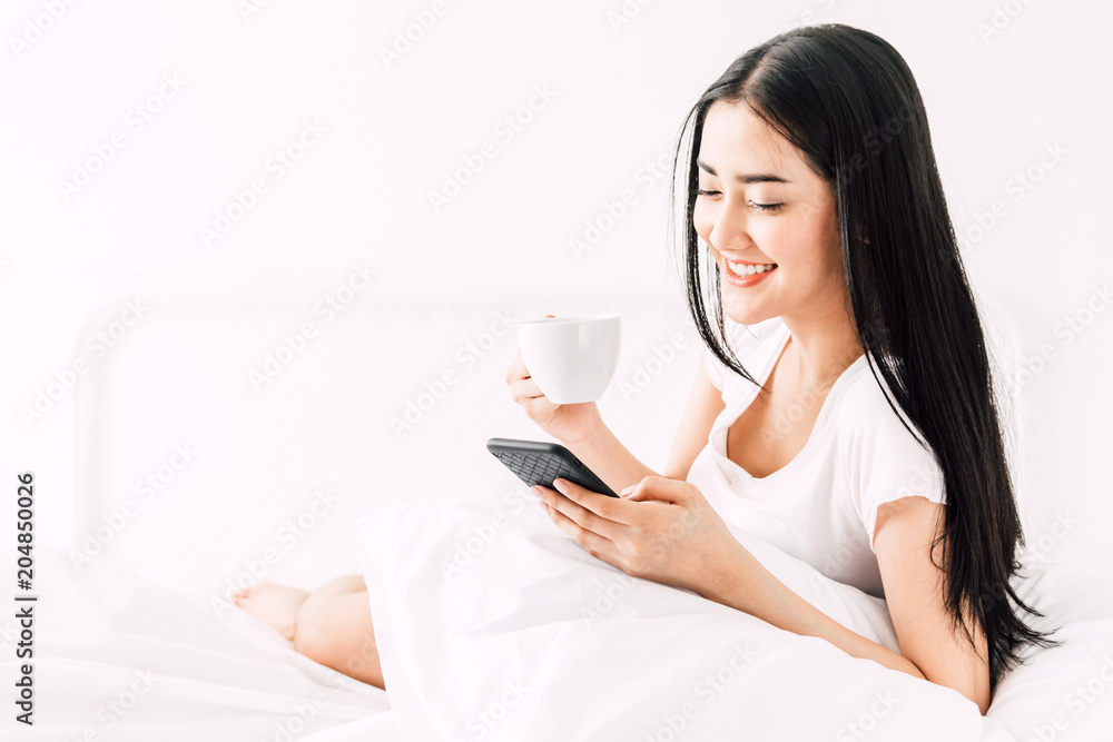 Happy woman relaxing and using smartphone on the bed at home.woman checking social apps with smartphone Happy woman relaxing and using smartphone on the bed at home.woman checking social apps with smartphone