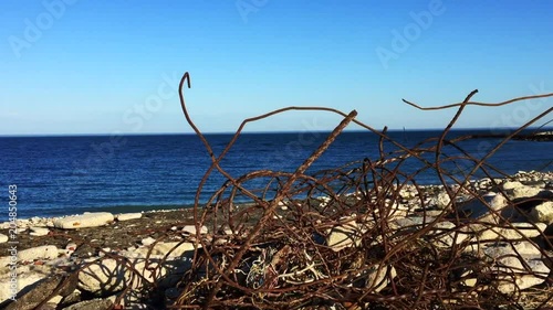 Tiltdown from blue sky to reveal beach with lake and gnarly abandoned old rusted steel sticking out of concrete photo