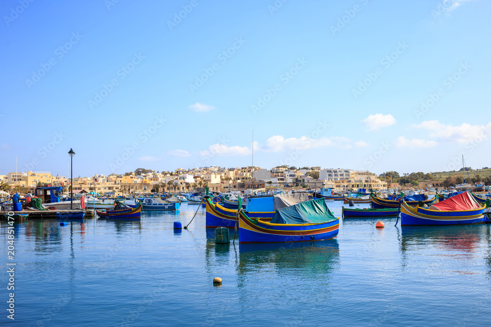 Marsaxlokk historic harbor full of wooden boats in Malta. Blue sky and village background.