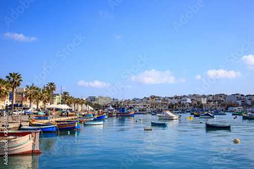 Marsaxlokk historic port full of wooden boats in Malta. Blue sky and village background.