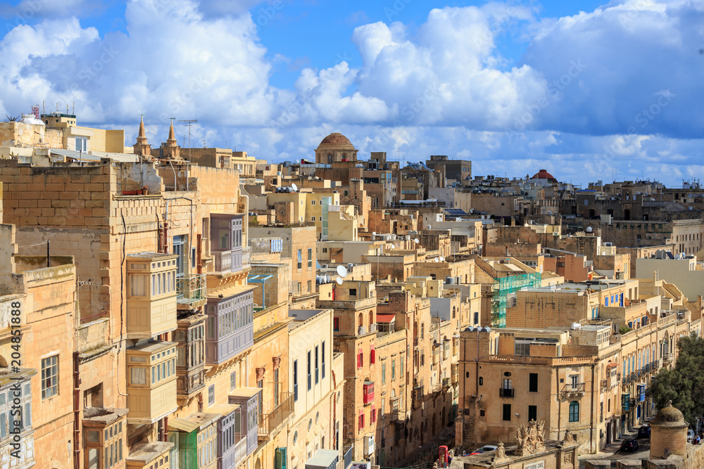 Malta, Valletta. Capital with tall traditional limestone buildings, under a blue sky with few clouds.
