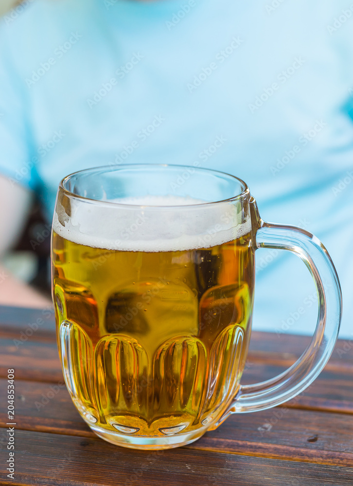 Mug of light beer is on a wooden table in a tavern