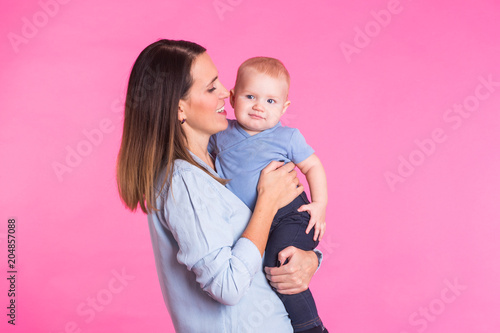 Loving mother playing with her baby boy on pink background