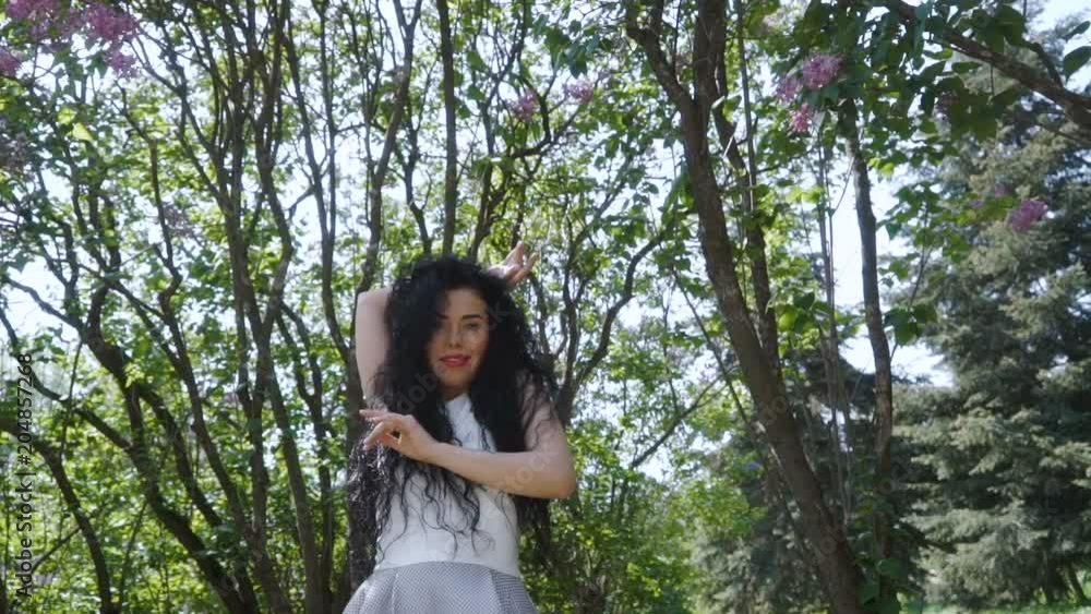 Beautiful brunete gently moving her hands standing at green trees background Beautiful brunete gently moving her hands standing at green trees background