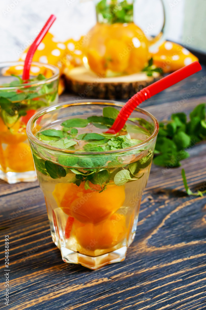 Summer cold drinks. Delicious refreshing drink with apricot and mint in glasses on a wooden table. Compote of fruits. Selective focus. Summer cold drinks. Delicious refreshing drink with apricot and mint in glasses on a wooden table. Compote of fruits. Selective focus.