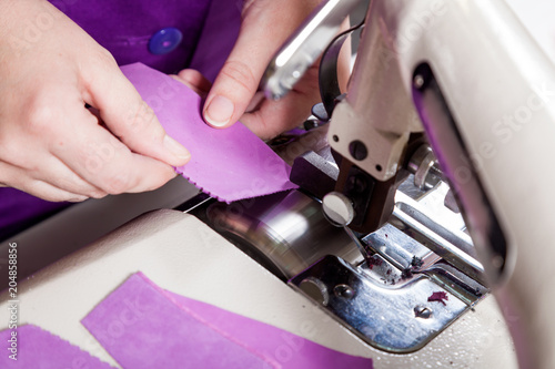 Close-up of a young woman working as a seamstress in a purple unifrome sews genuine leather children's shoes on a sewing machine, top view photo