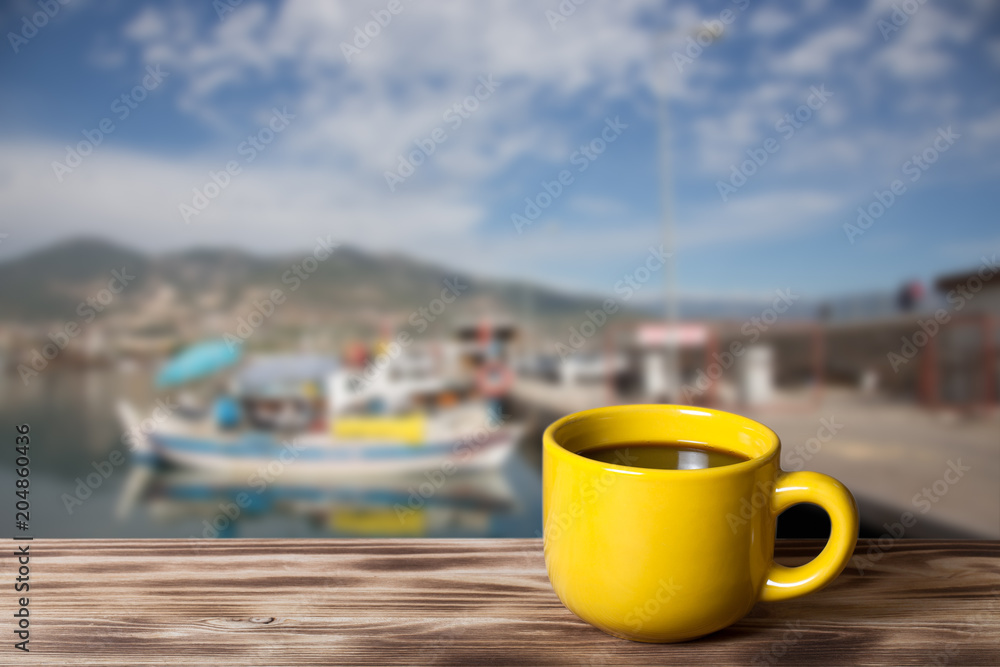 Yellow cup with tea on wooden table opposite a defocused background. Collage. Selective focus Yellow cup with tea on wooden table opposite a defocused background. Collage. Selective focus