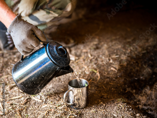 Wasser mit einer alten Blech Kaffekanne in einen Becher gießen 