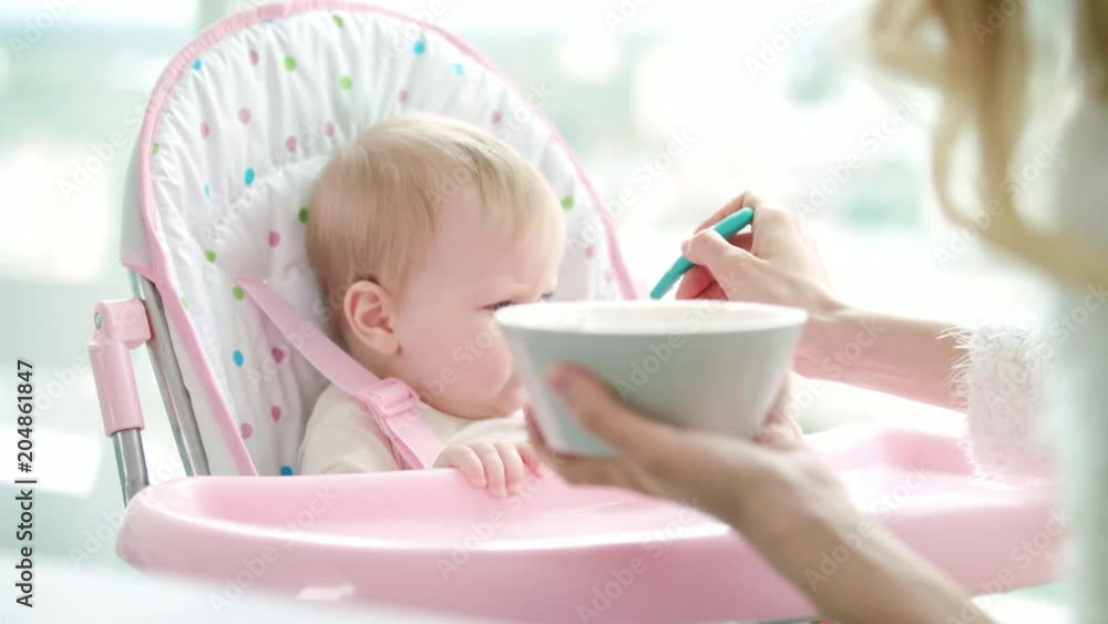 Mother feeding child with baby food. Woman feeding kid with spoon. Cute baby girl eating from porridge bowl. Toddler girl eat pureed food. Mom feed daughter Mother feeding child with baby food. Woman feeding kid with spoon. Cute baby girl eating from porridge bowl. Toddler girl eat pureed food. Mom feed daughter