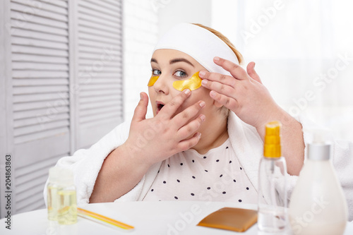 Great eye mask. Alert overweight woman wearing a bathrobe and making an eye mask
