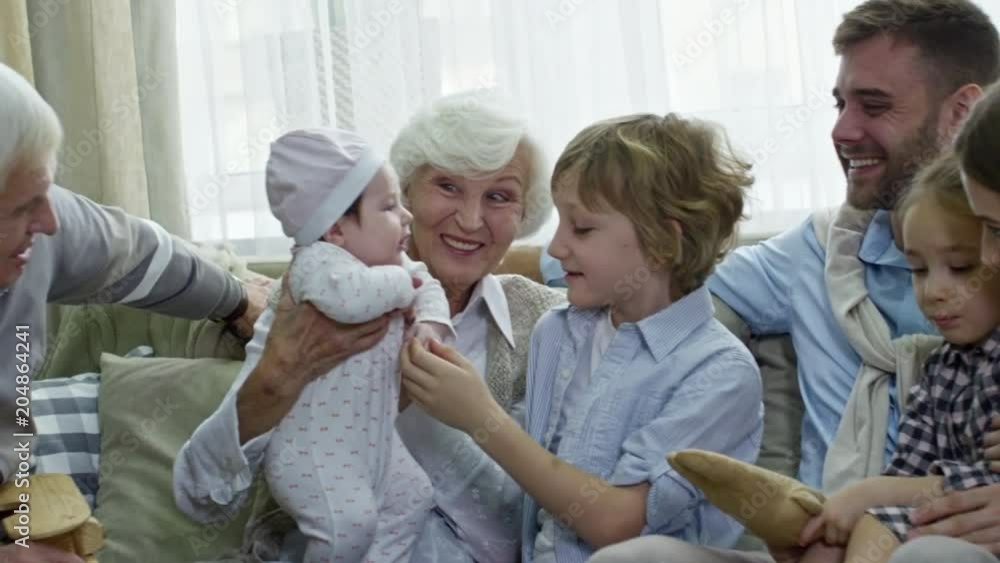 PAN of big family of grandparents, parents and children cooing over cute baby PAN of big family of grandparents, parents and children cooing over cute baby