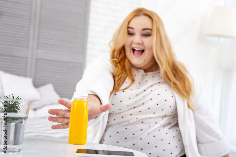 My breakfast. Joyful overweight woman smiling and taking her juice My breakfast. Joyful overweight woman smiling and taking her juice