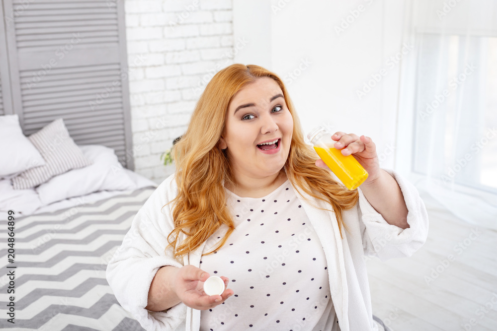 Healthcare. Alert overweight woman sitting on the couch and drinking her juice Healthcare. Alert overweight woman sitting on the couch and drinking her juice