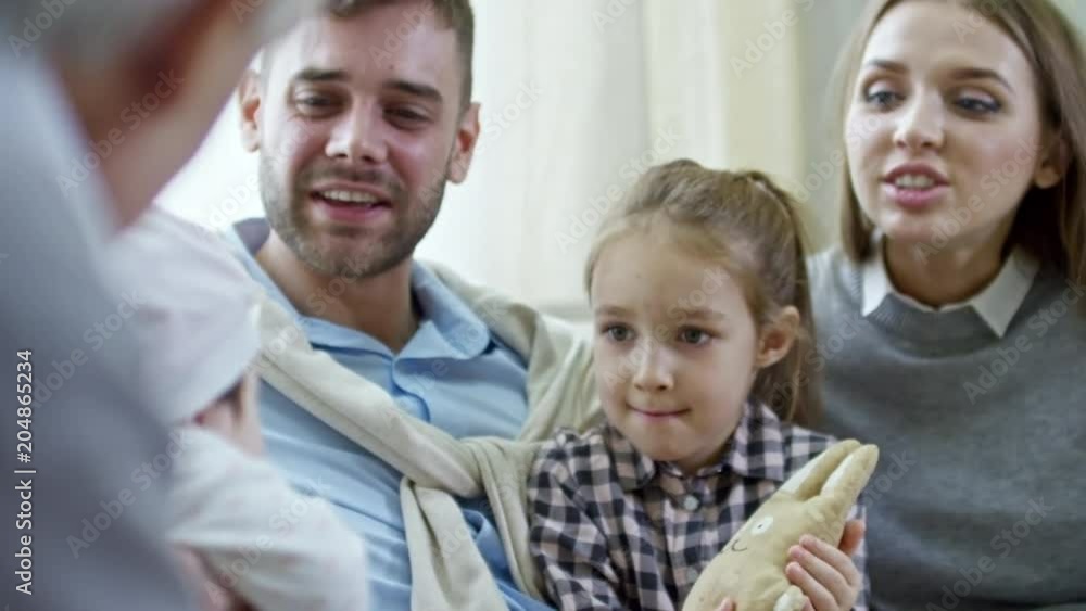 Medium shot of happy parents with elementary age girl laughing and cooing over cute baby held by grandparents Medium shot of happy parents with elementary age girl laughing and cooing over cute baby held by grandparents