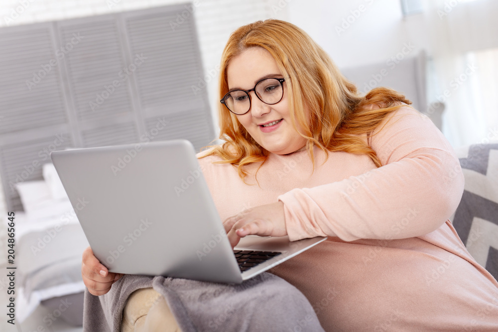 New project. Smiling overweight woman wearing glasses and working on her laptop New project. Smiling overweight woman wearing glasses and working on her laptop