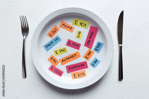 Colorful paper notes naming food additives on plate with fork and knife, food additive and unhealthy food concept.