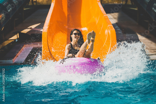 pretty woman in black bikini with legs up coming down on the inflatable ring by the slide in the aqua park. Summer Vacation. Enjoying suntan. Weekend on resort