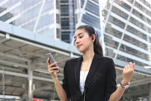 Relaxed young Asian woman listening music with mobile smart phone in modern city.