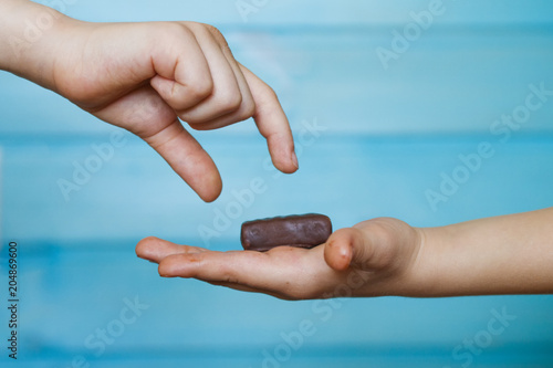 The child holds a chocolate candy in the palm of his hand, sharing it with his friend