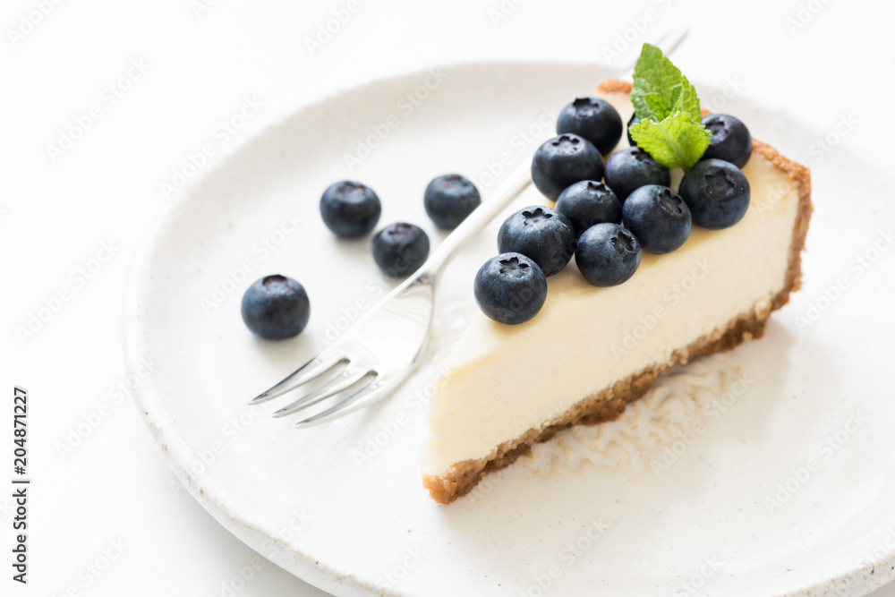 Slice of cheesecake with blueberries and mint leaf on white. Closeup view, selective focus. New York cheesecake Slice of cheesecake with blueberries and mint leaf on white. Closeup view, selective focus. New York cheesecake