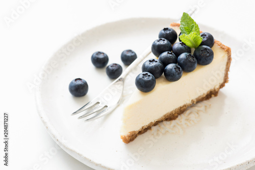 Slice of cheesecake with blueberries and mint leaf on white. Closeup view, selective focus. New York cheesecake