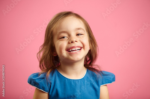 Cheerful little girl with charming smile and hearty laugh on pink isolated background, expresses heartfelt emotions of joy, is in a good mood. photo