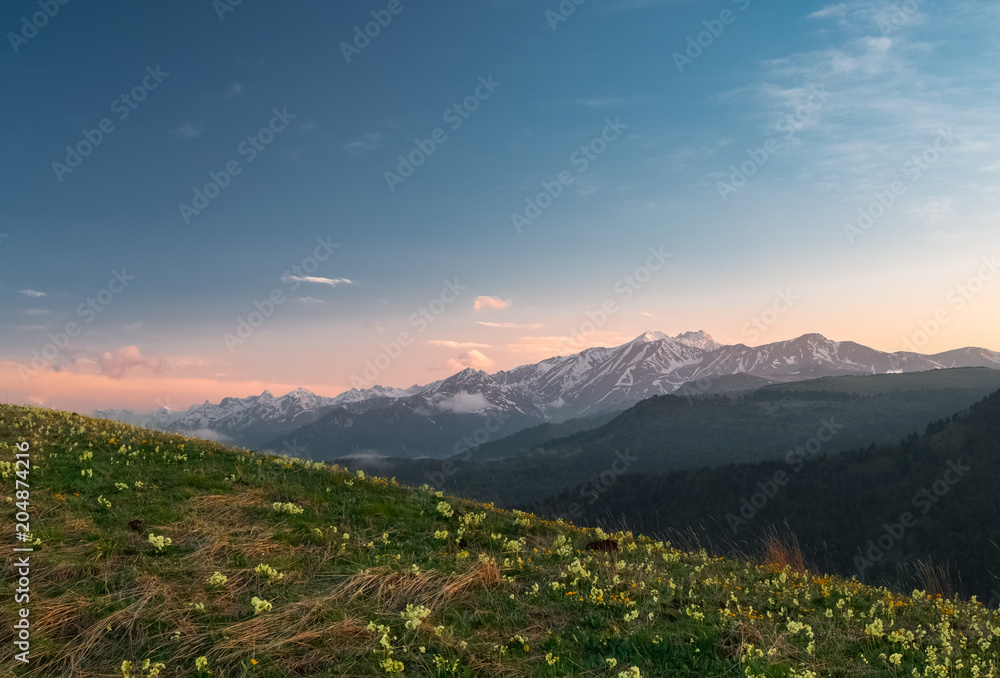 mountain ranges of the Karachay-Cherkess Republic with clouds at sunset with a green meadow with flowers