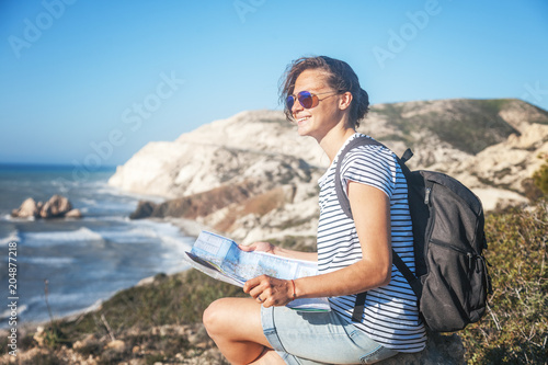 girl young woman traveler with a backpack and map in hand walks on the background of a beautiful landscape, the sea and the hills,