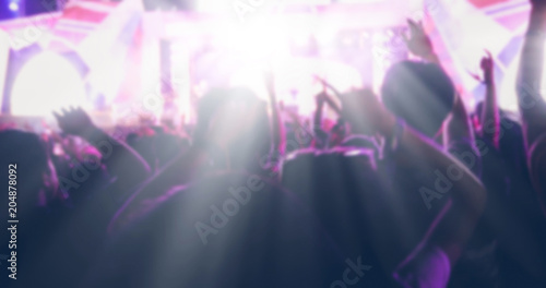 blurry of silhouettes of concert crowd at Rear view of festival crowd raising their hands on bright stage lights © tuiphotoengineer