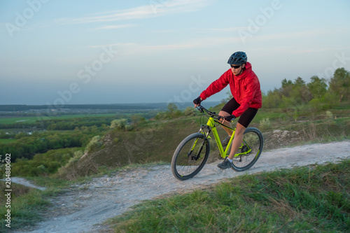 A cyclist in a red jacket rides a bike along the mountain path. The concept of extreme sports. Mountain bike.