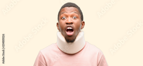 Injured african black man wearing neck brace stressful, terrified in panic, shouting exasperated and frustrated. Unpleasant gesture. Annoying work drives me crazy