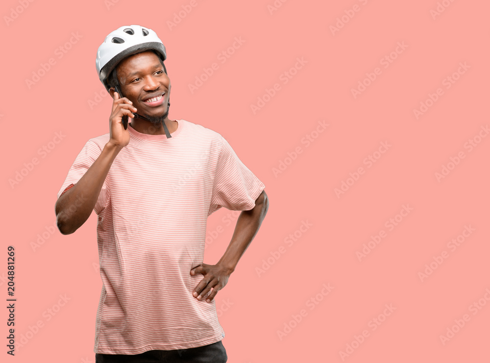 Black man wearing bike helmet happy talking using a smartphone mobile phone Black man wearing bike helmet happy talking using a smartphone mobile phone