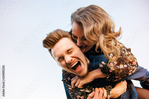 Fototapeta The guy rolls his beloved girl on his back against the backdrop of sky