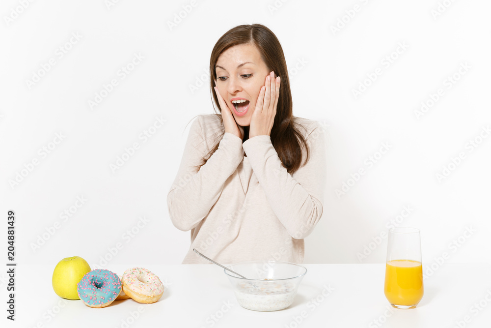 Young woman sitting at table breakfast with cereals and milk, orange juice in glass, donuts isolated on white background. Proper nutrition, delicious tasty food, healthy lifestyle. Area to copy space. Young woman sitting at table breakfast with cereals and milk, orange juice in glass, donuts isolated on white background. Proper nutrition, delicious tasty food, healthy lifestyle. Area to copy space.
