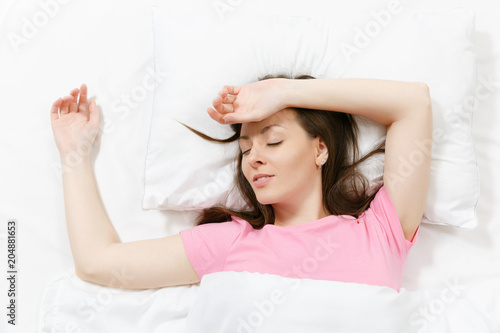 Top view of head of happy brunette young woman lying in bed with white sheet  pillow  blanket. Sleeping pretty female spending time in room. Rest  relax  good mood concept. Copy space to advertisement