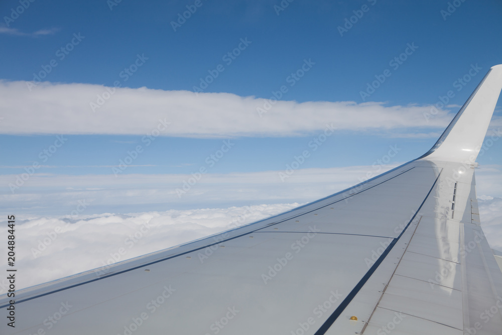 View of the plane's wing and landscape with blue sky and clouds from above. View of the plane's wing and landscape with blue sky and clouds from above.
