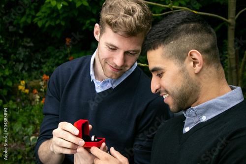 Engagement proposal betwen two gay men as one man proposes with an engagement ring in red box photo