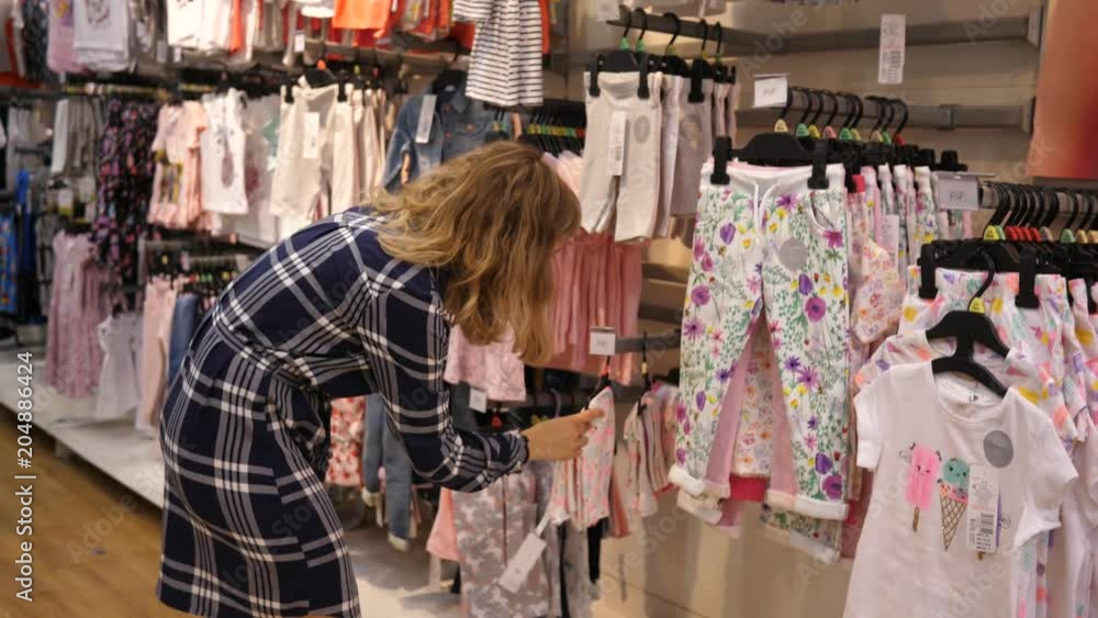 Young mother shopping choosing clothes in a store department for children Young mother shopping choosing clothes in a store department for children