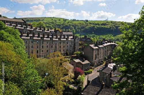 A view of the winding streets and tall stone houses in hebden bridge se in the surrounding west yorkshire countryside with pennine hills and bright summer trees with blue cloudy sky photo