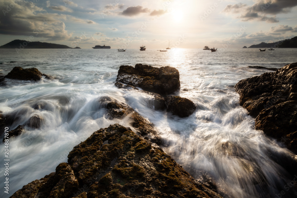 By the sea during the time of sunset with rock and the crashing waves. Beautiful natural summer seascape