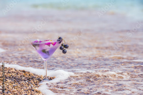 refreshing summer drink in a glass on the beach, sparkling drops of water and pebbles in the surf line. Art photo with the mood of summer and rest. very selective soft focus
