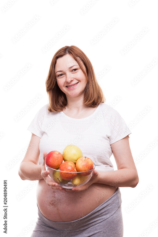 Pregnant woman smiling to the camera holds an glass bowl with fruits in her hands. Isolated over white background Pregnant woman smiling to the camera holds an glass bowl with fruits in her hands. Isolated over white background