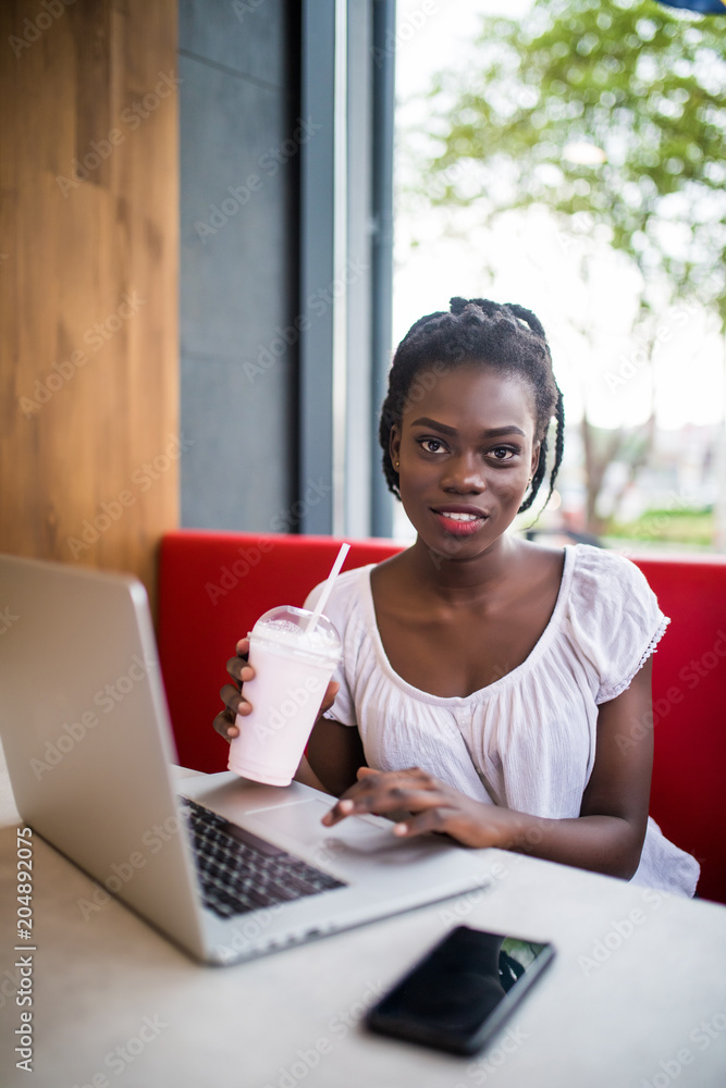 Young afro american woman relaxing, browse in internet laptop, drink milkshake in cafe Young afro american woman relaxing, browse in internet laptop, drink milkshake in cafe