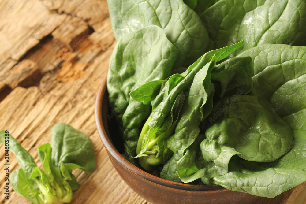 Fresh green leaves of spinach in a bowl on old wooden background. Fresh green leaves of spinach in a bowl on old wooden background.